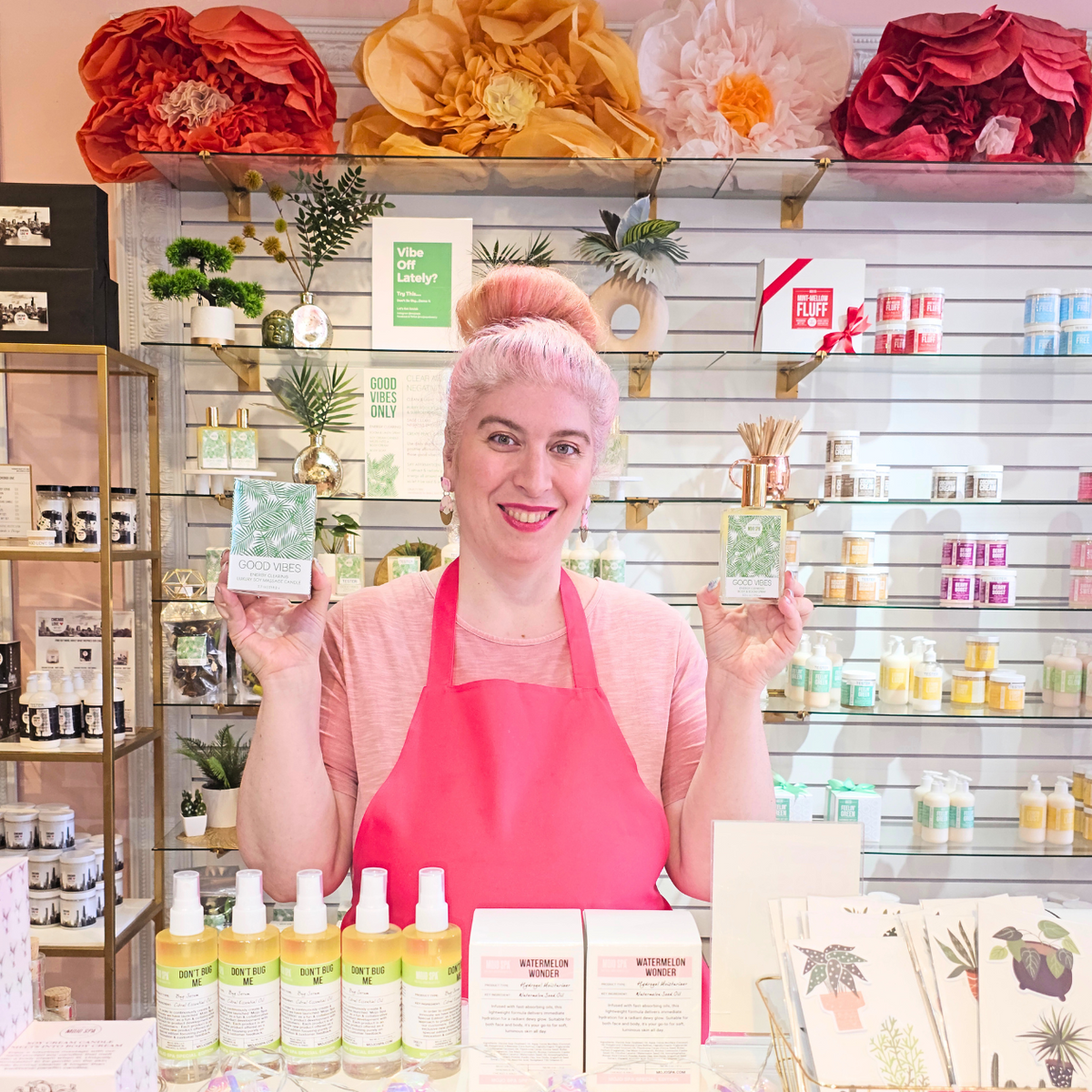 Amanda in a pink apron holding up products in the Mojo Spa shop