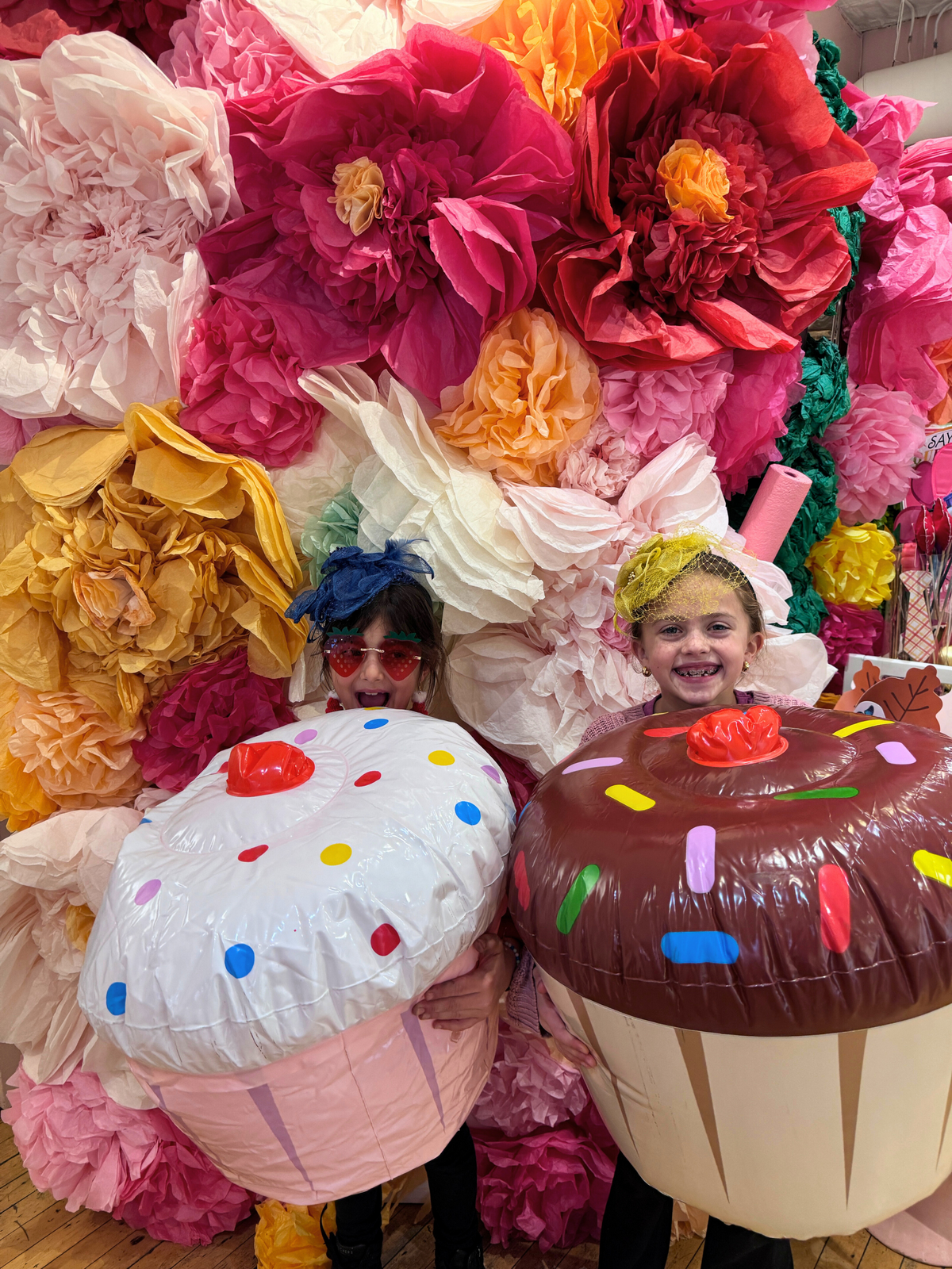 Two party guests in inflatable cupcake costumes in front of the flower wall