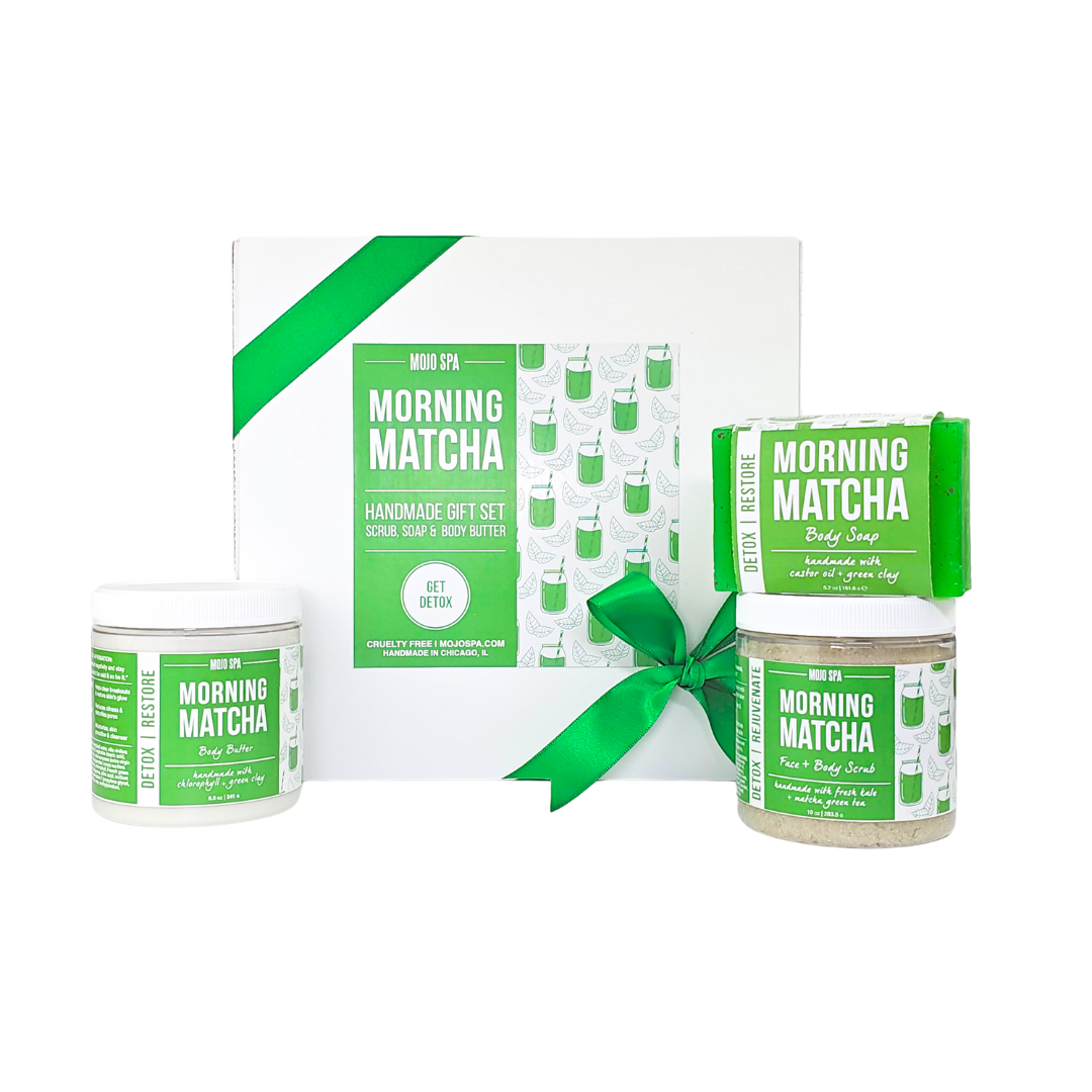 The contents in front of the box, a body butter jar on the left and a soap bar resting on a scrub jar on the right