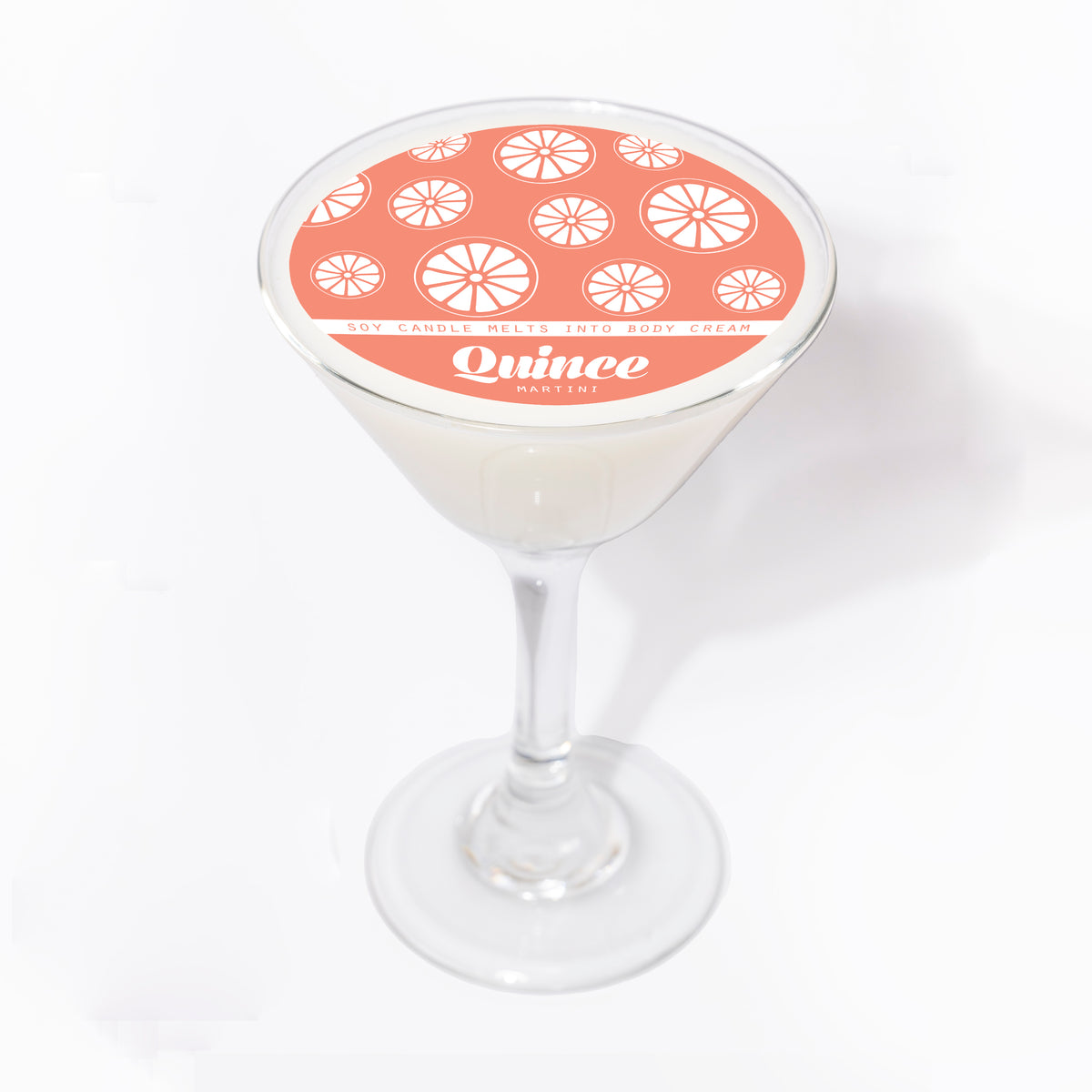 Quince Martini soy massage candle in a clear martini glass, white wax topped with a round coral label of citrus slices