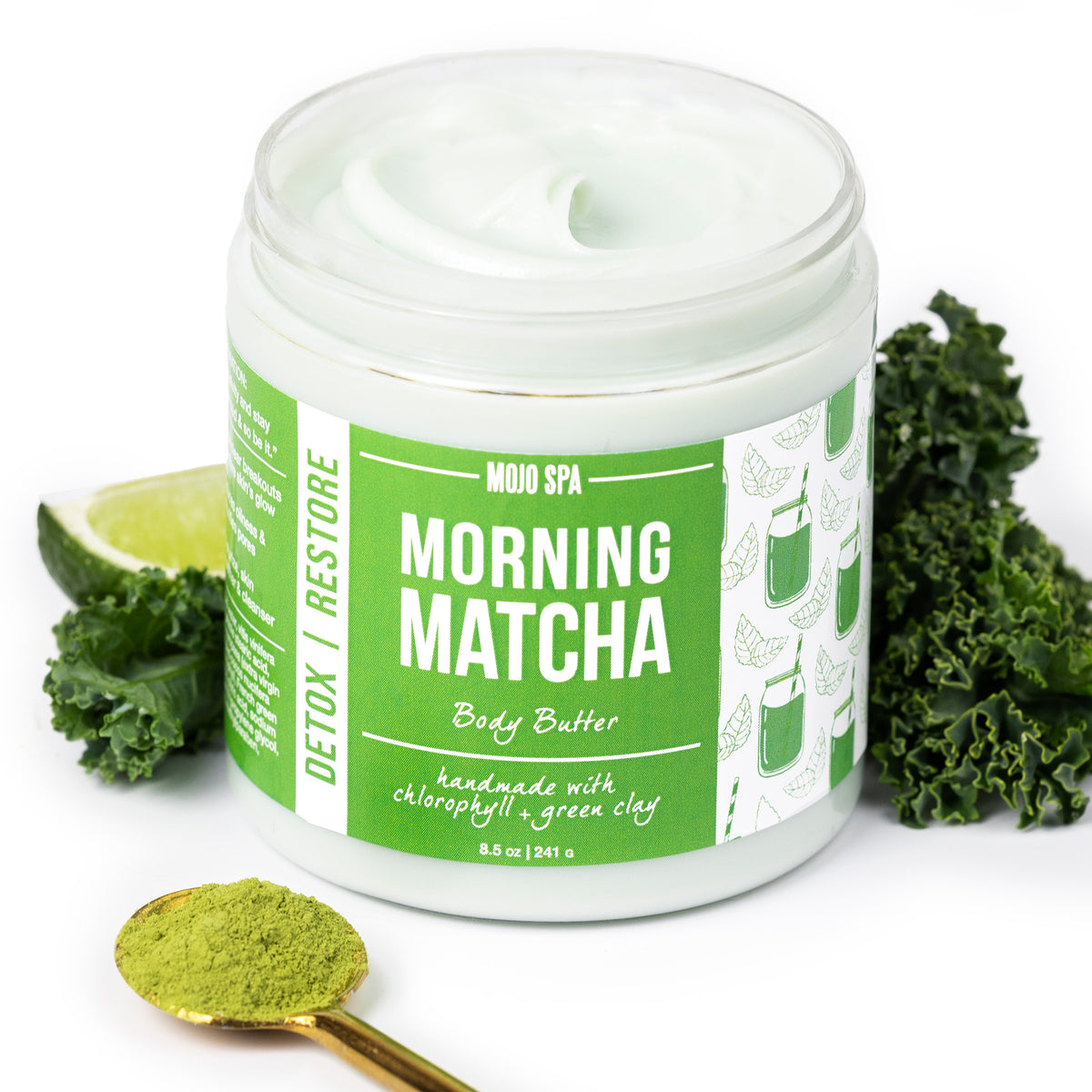 The jar surrounded by kale, a lime wedge and a gold spoon of matcha powder