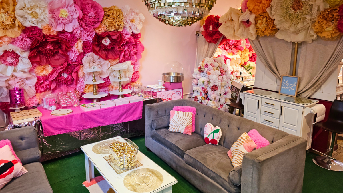 The party lounge, with gray couches, a pink catering table and a wall of paper flowers