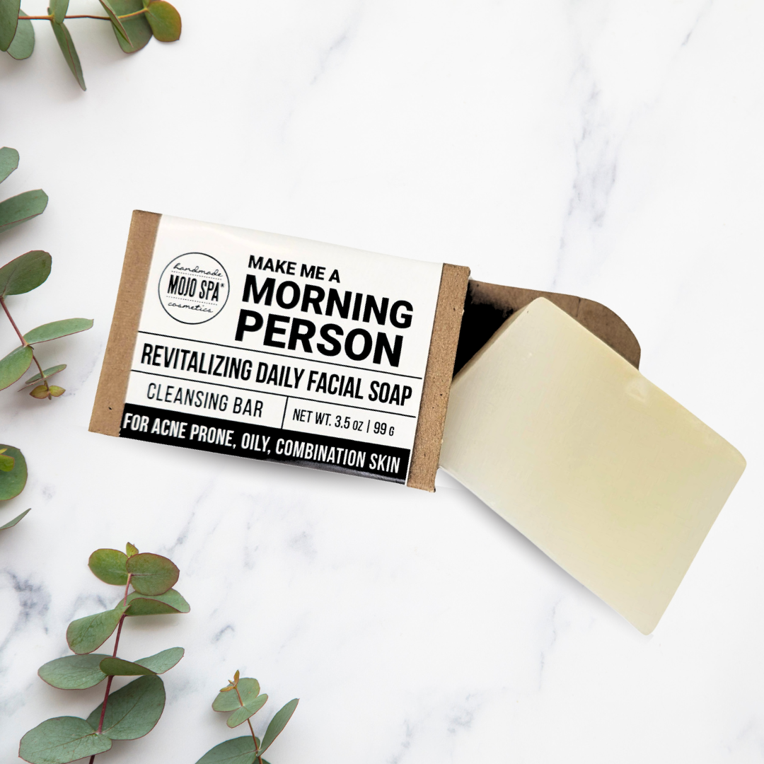 The wrapped bar with the soap sliding out, on white marble among eucalyptus leaves