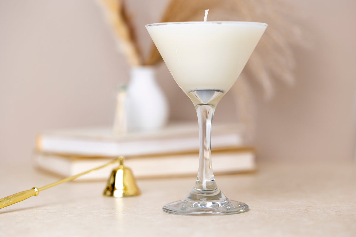 The unlit candle in its martini glass in front of a vase of dried pampas grass, with books and a gold snuffer