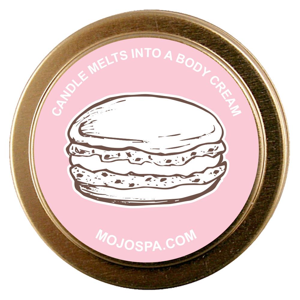The gold tin lid with a pink centre, a drawing of a stacked macaron and the line Candle melts into a body cream, with mojospa.com