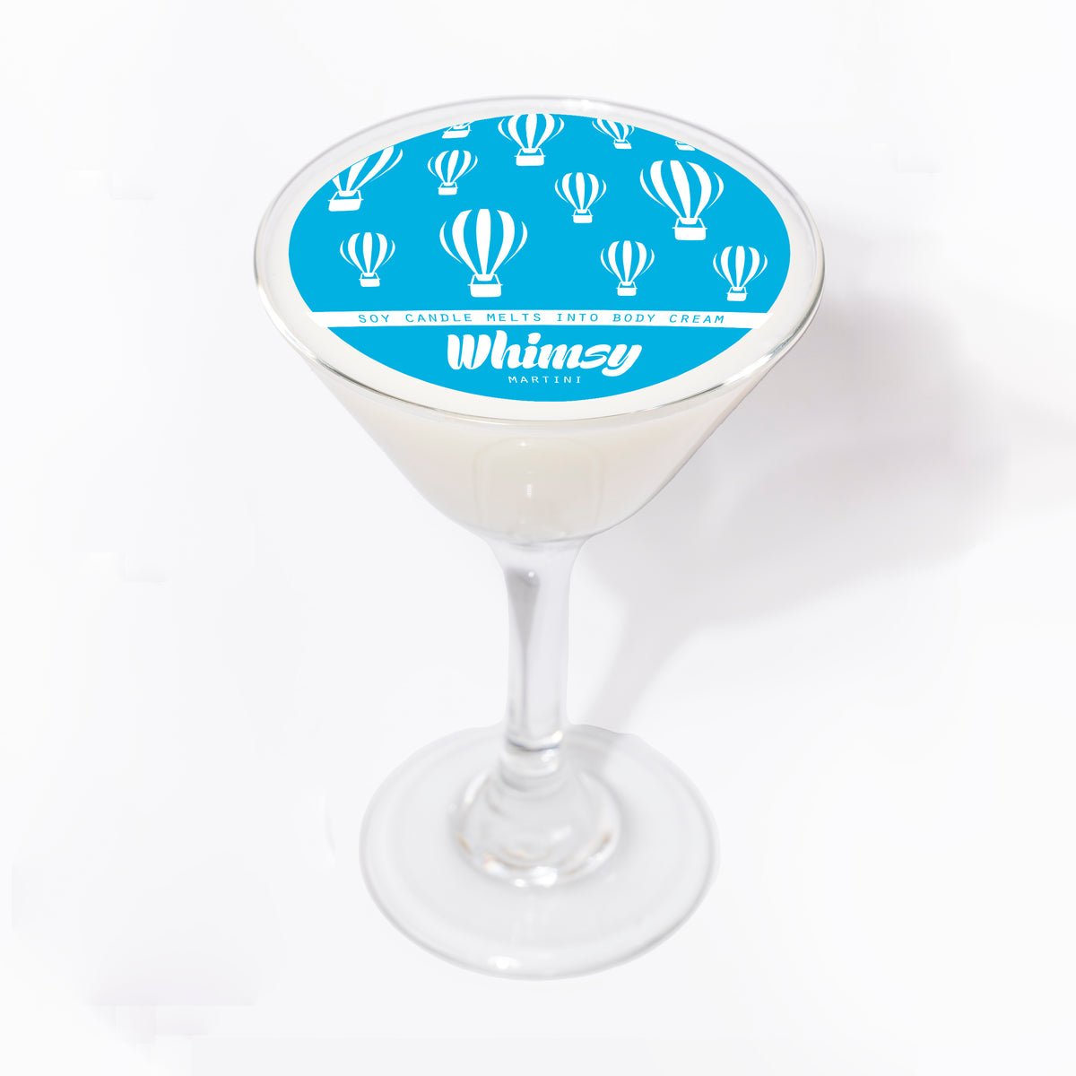 Whimsy Martini soy massage candle in a clear martini glass, white wax topped with a round blue label of hot air balloons