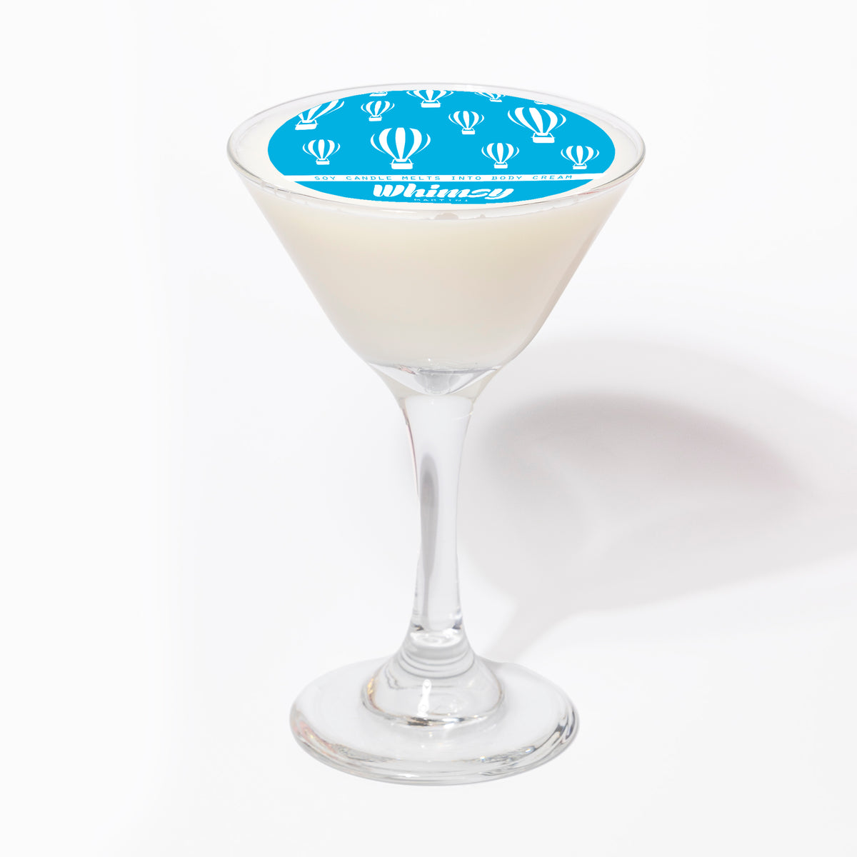 The candle from the side, showing the white wax in the glass beneath the blue Whimsy label