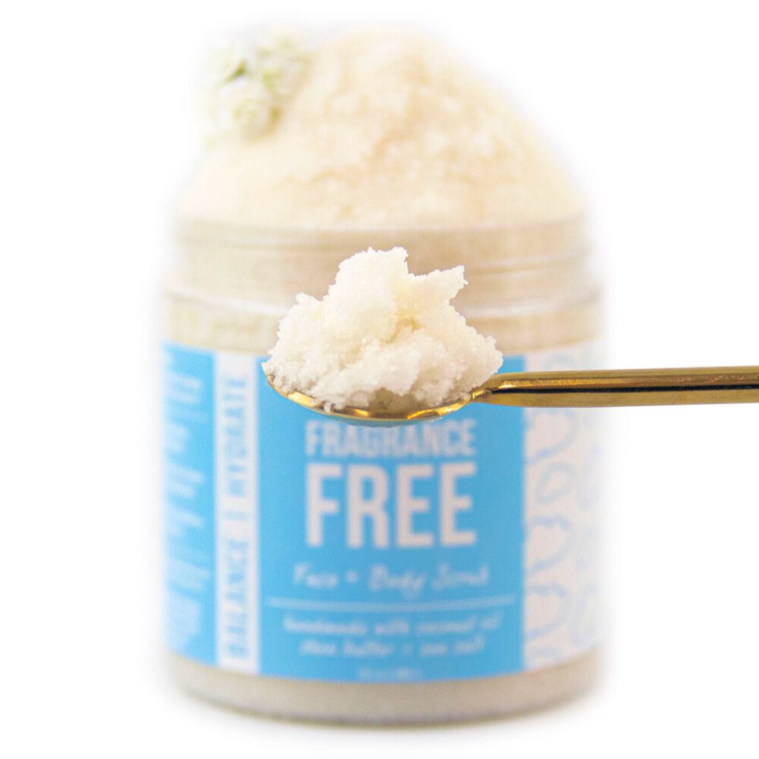 A gold spoon lifting a scoop of cream-coloured scrub in front of the blurred jar