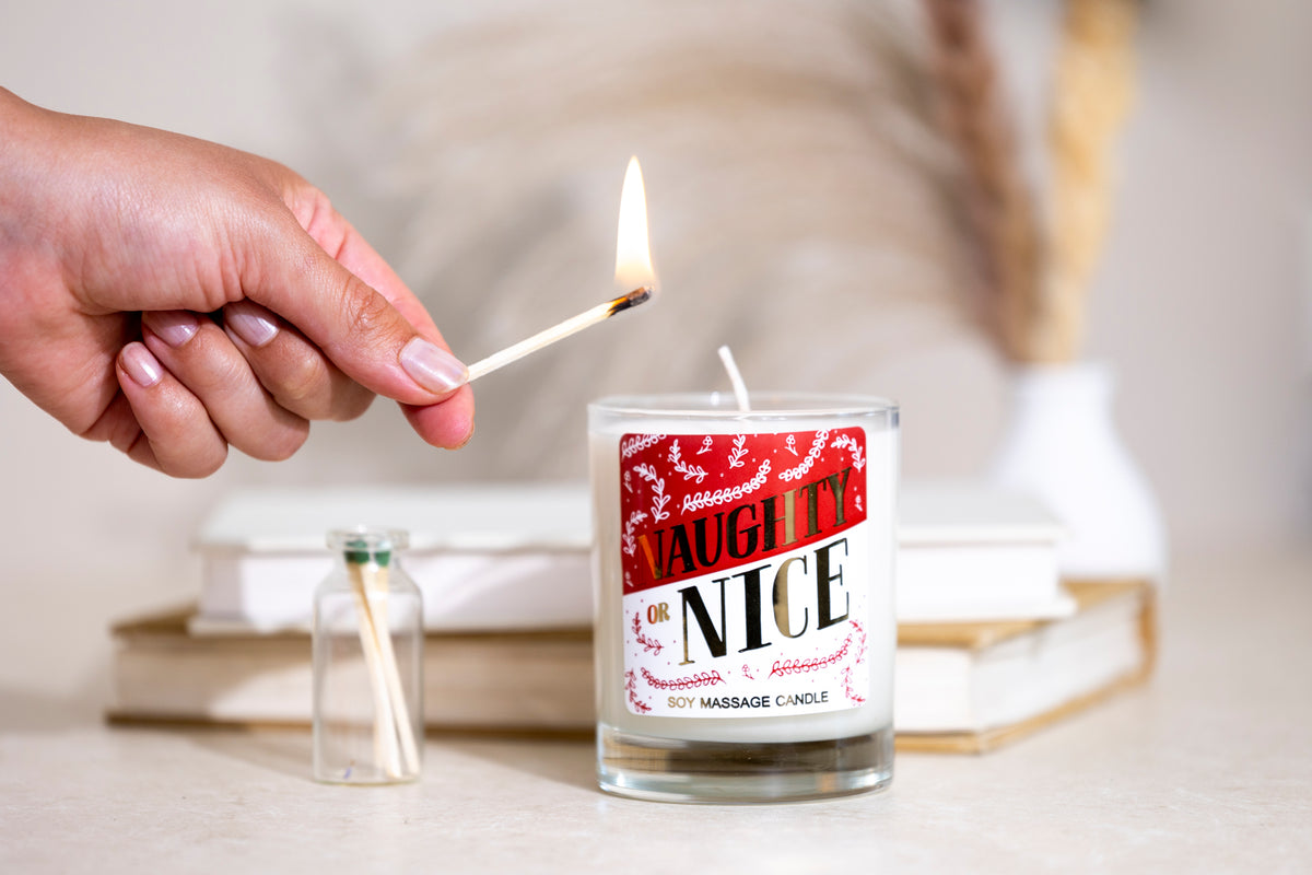 A hand lighting the candle with a match, with a small jar of matches and books in the background