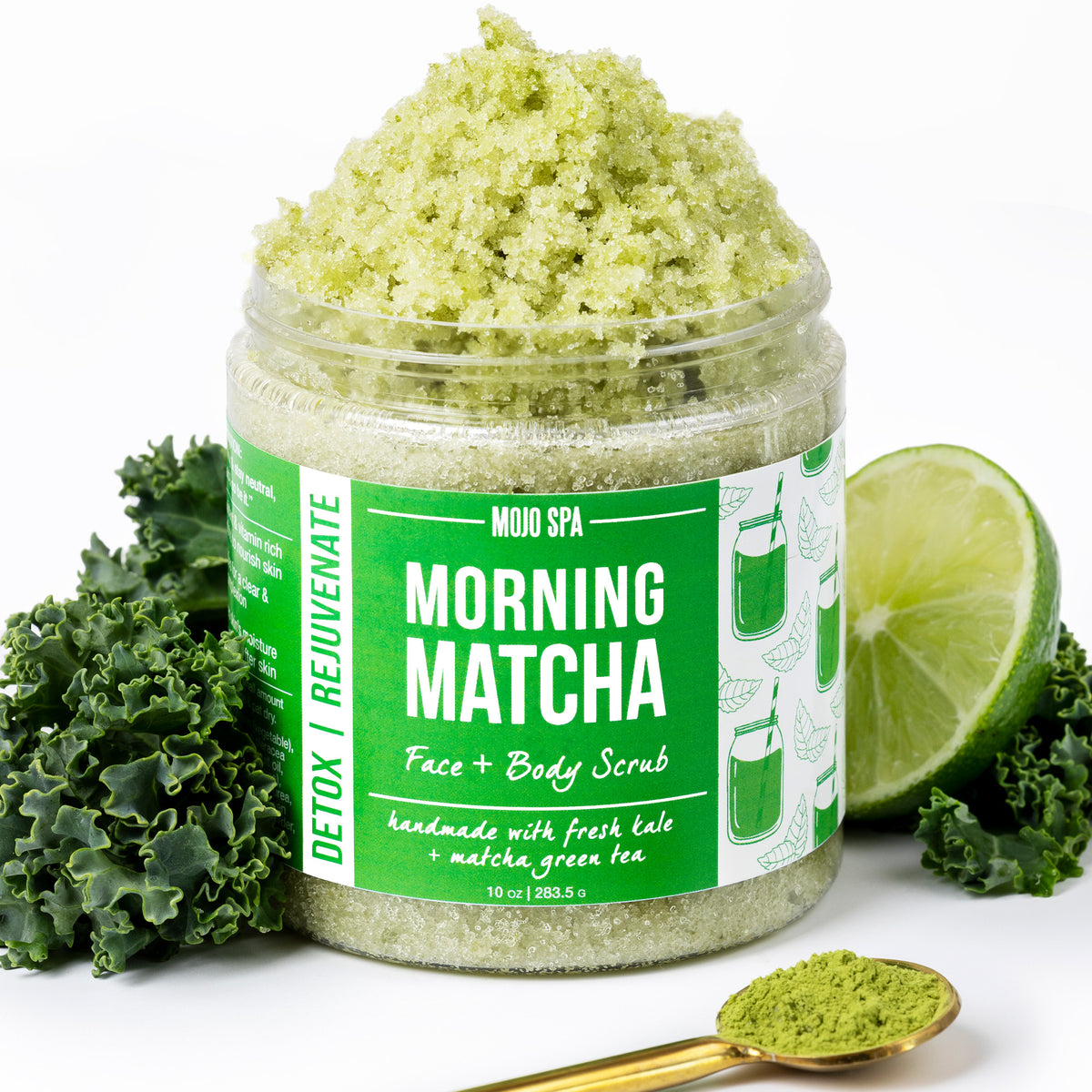 The jar with scrub piled high, beside kale, a lime half and a gold spoon of matcha powder