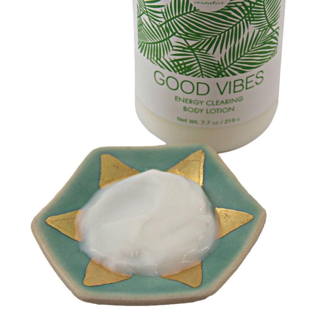 A dab of white lotion on a hexagonal teal and gold ceramic dish, the bottle above